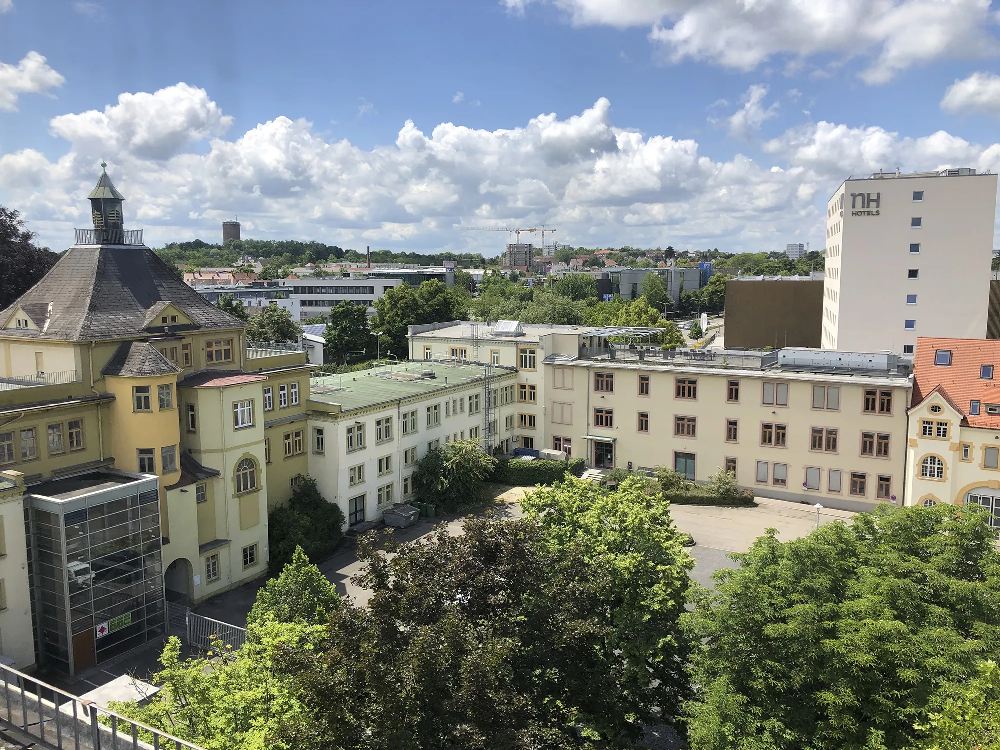 Luftaufnahme des Caro Carrés inklusive Innenhof. Im Vordergrund große grüne Bäume, im Hintergrund ein Hotelgebäude sowie viele andere Gebäude.