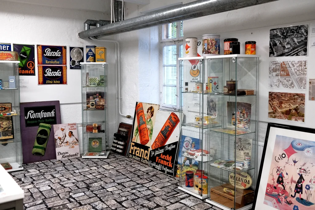 Ein heller Raum mit mehreren Vitrinen die Produkten einer ehemaligen Kaffe-Rösterei austellen. Zwischen den Vitrinen stehen und hängen verschiedene Werbeplakate und Schilder an der Wand.
