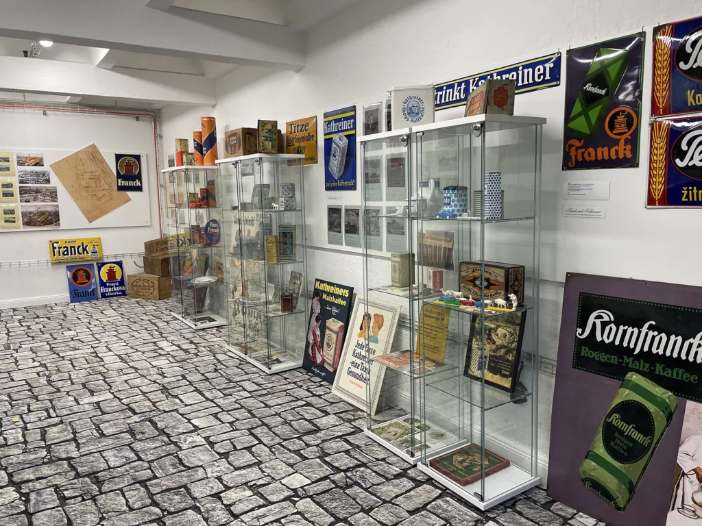Ein heller Raum mit mehreren Vitrinen die Produkten einer ehemaligen Kaffe-Rösterei austellen. Zwischen den Vitrinen stehen und hängen verschiedene Werbeplakate und Schilder an der Wand.