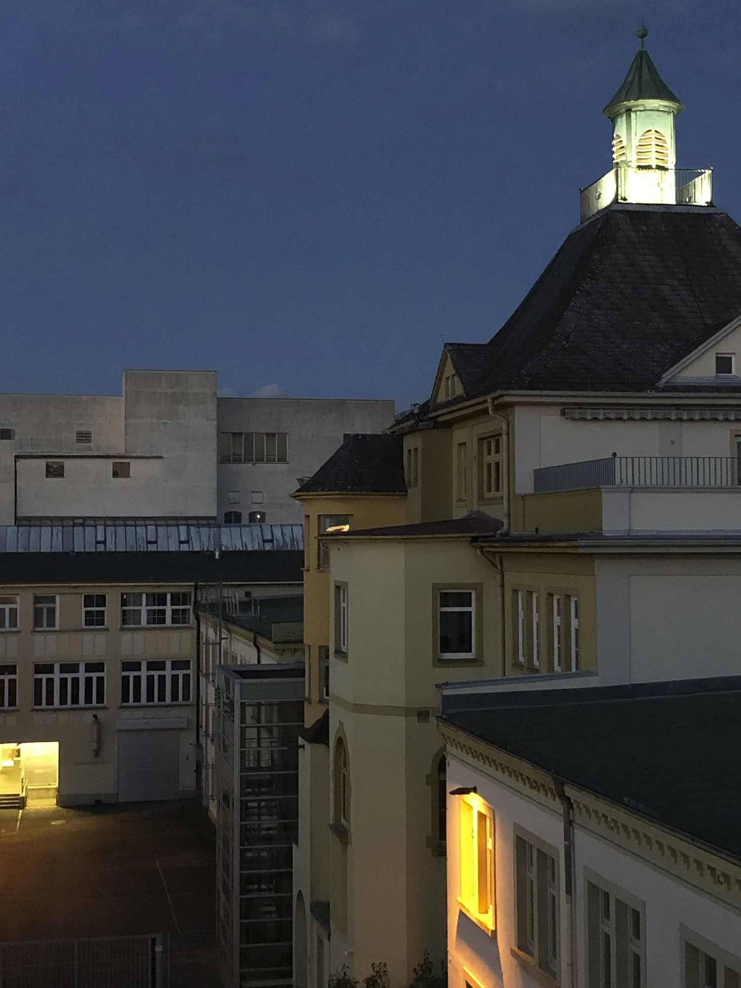 Abendaufnahme eines historischen Gebäudes mit beleuchtetem Turm und gelb erleuchteten Fenstern, umgeben von weiteren Gebäuden im Innenhof des caro carrés.