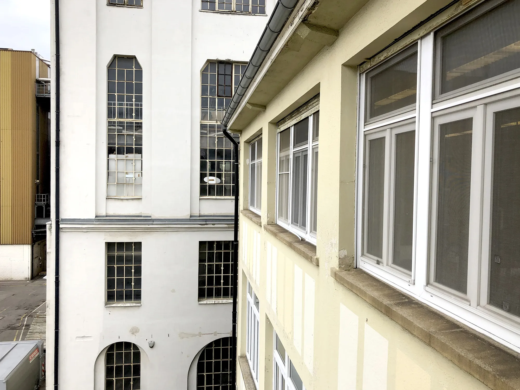 Blick auf die Fassade zweier angrenzender Industriegebäude im Caro Carré mit großen rechteckigen und hohen, schmalen Fenstern, gelber und weißer Außenwand.