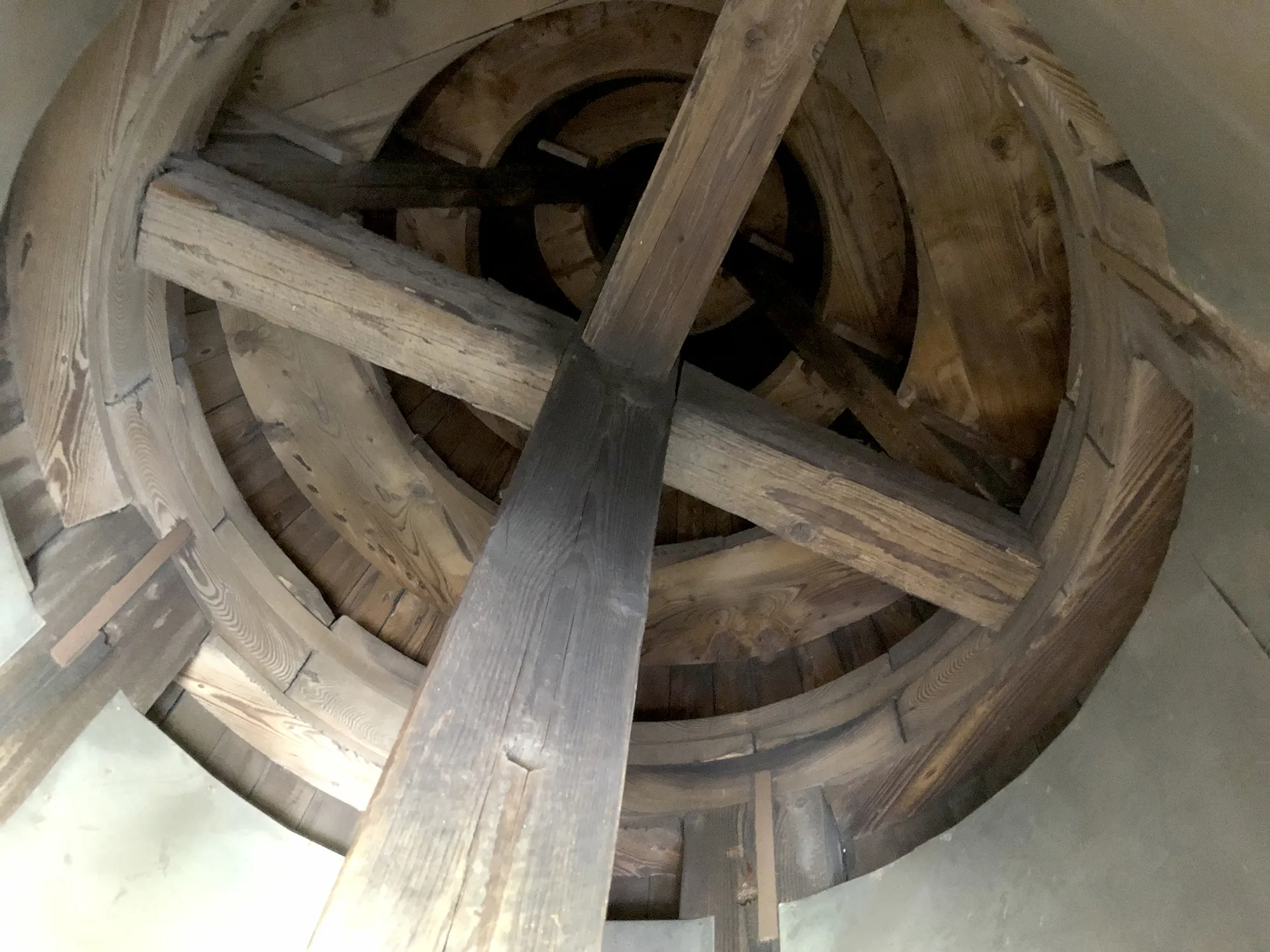 Holzkonstruktion im Inneren einer runden Glockenturmspitze, bestehend aus mehreren kreisförmigen und gekreuzten Balken.
